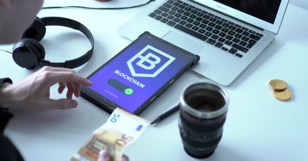 Blockchain-Transaktion auf Tablet neben Laptop und Euro-Scheinen in Nahaufnahme